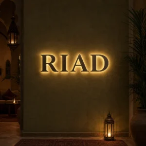 Lettres murales rétroéclairées formant le mot RIAD sur un mur vert olive