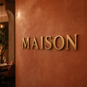 Lettres dorées en laiton brossé formant le mot MAISON sur un mur terracotta